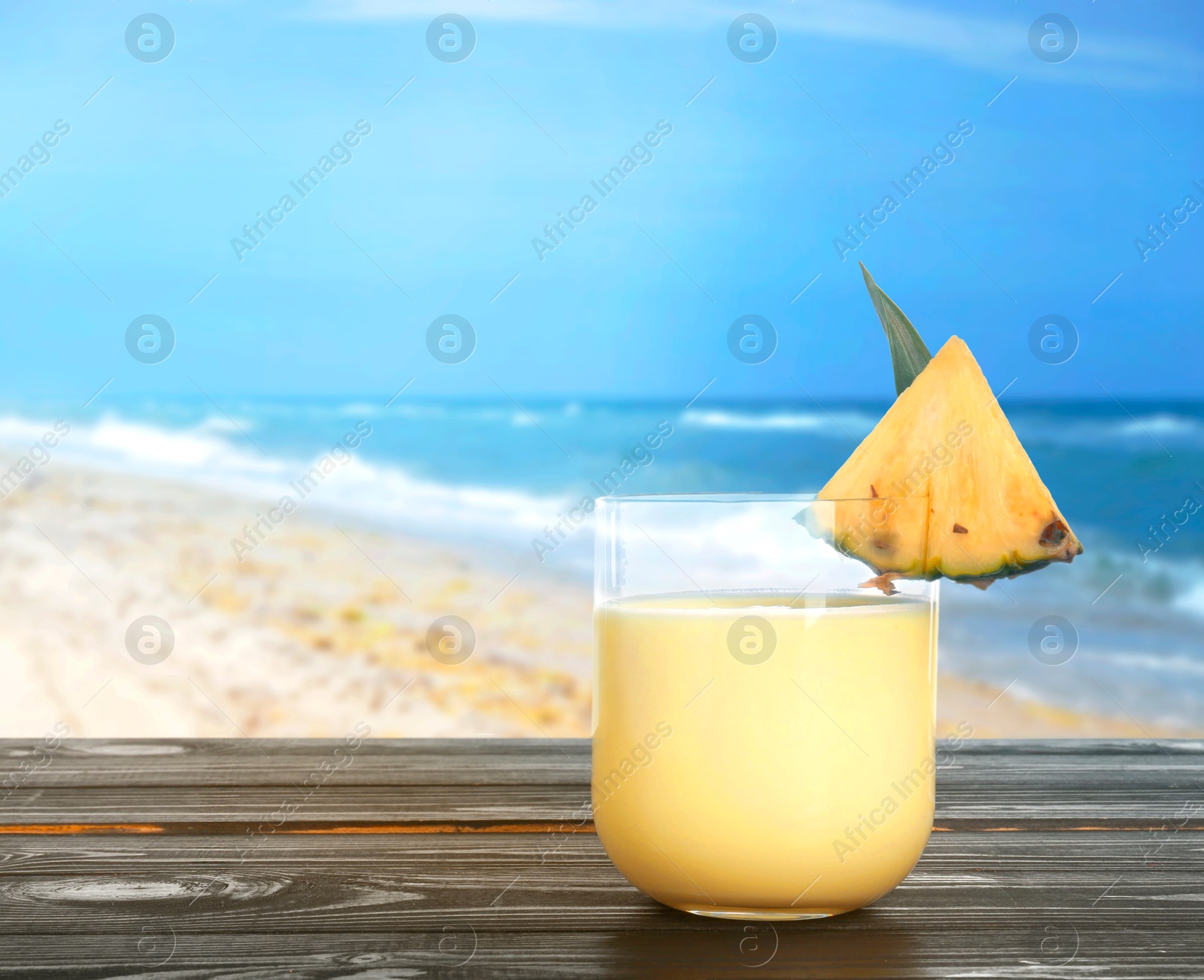 Image of Tasty pineapple cocktail or smoothie in glass on wooden table against seascape. Space for text