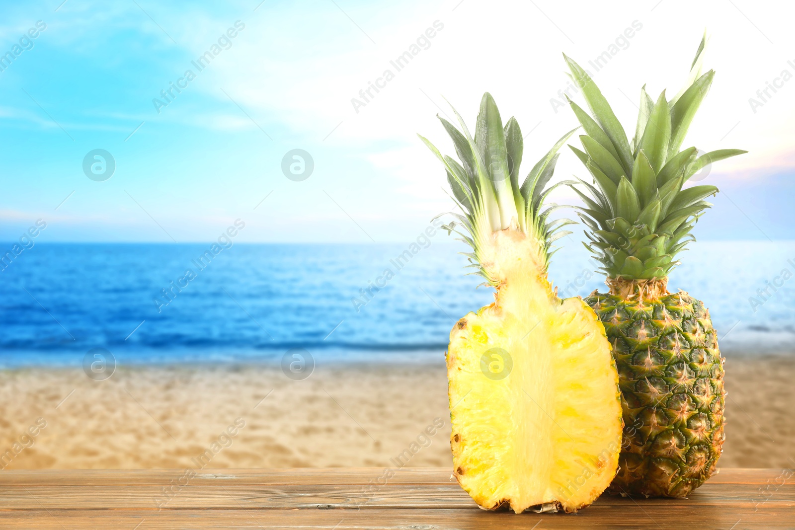 Image of Fresh ripe pineapples on wooden table against seascape. Space for text