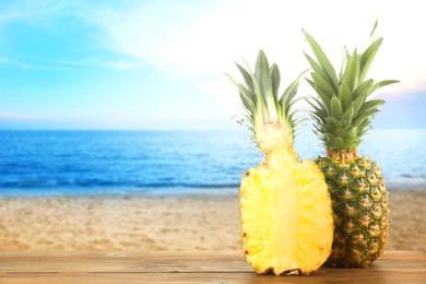 Image of Fresh ripe pineapples on wooden table against seascape. Space for text