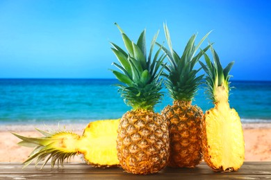 Image of Fresh ripe pineapples on wooden table against seascape. Space for text