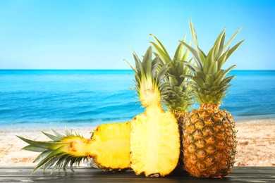 Image of Fresh ripe pineapples on wooden table against seascape. Space for text