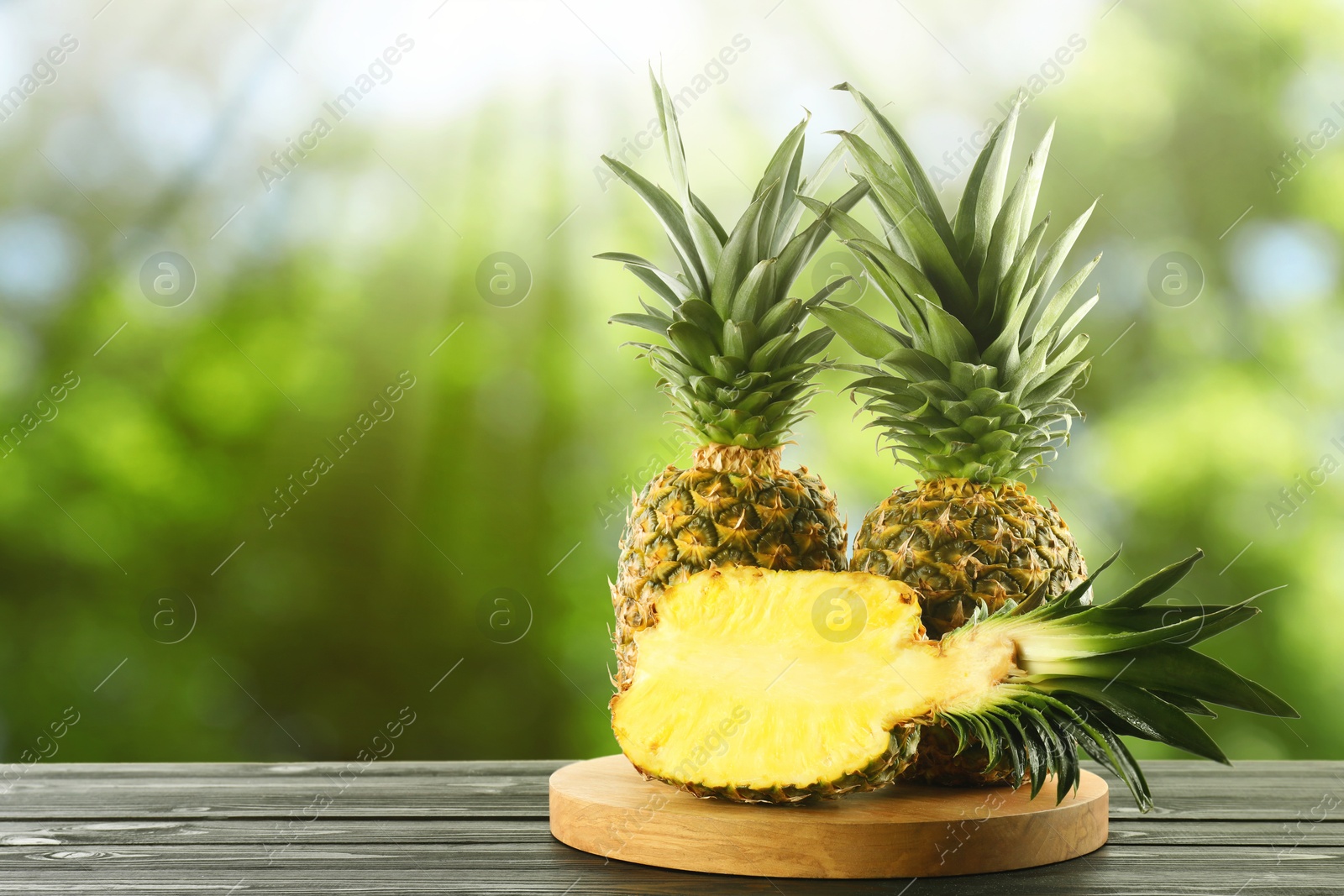 Image of Fresh ripe pineapples on wooden table outdoors. Space for text