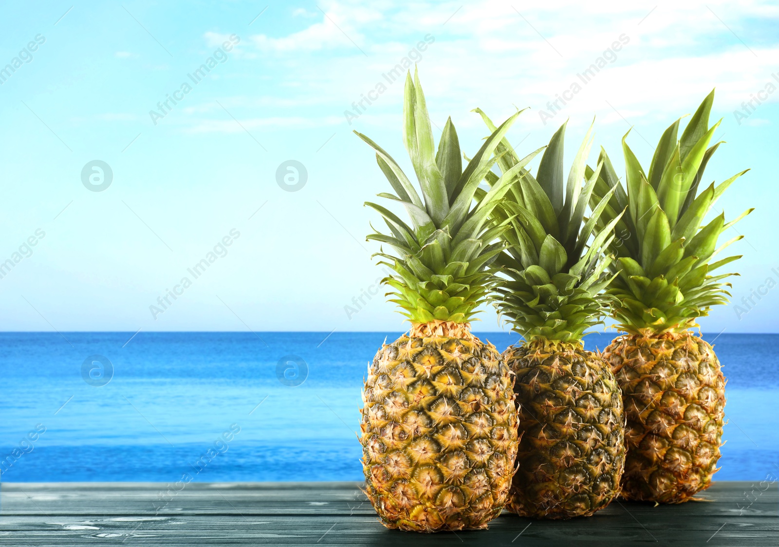 Image of Fresh ripe pineapples on wooden table against seascape. Space for text