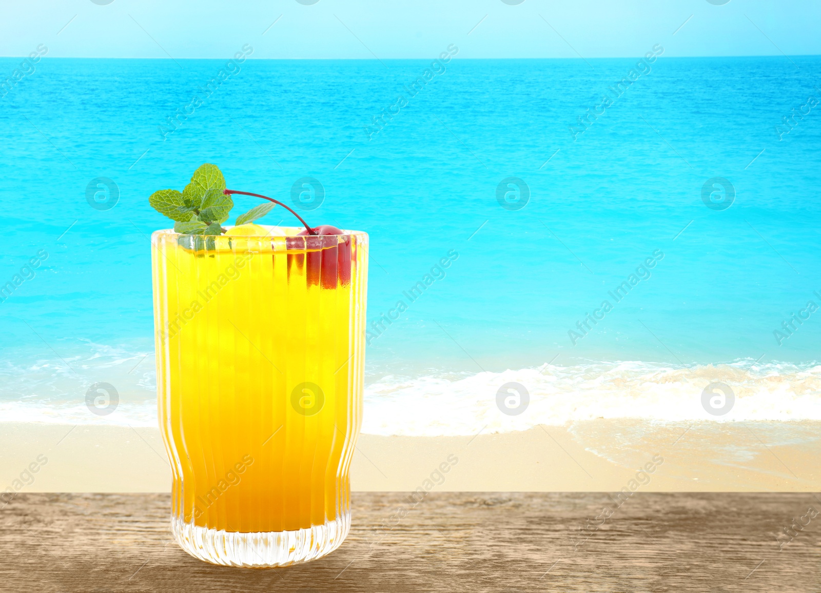 Image of Tasty pineapple cocktail in glass on wooden table against seascape. Space for text