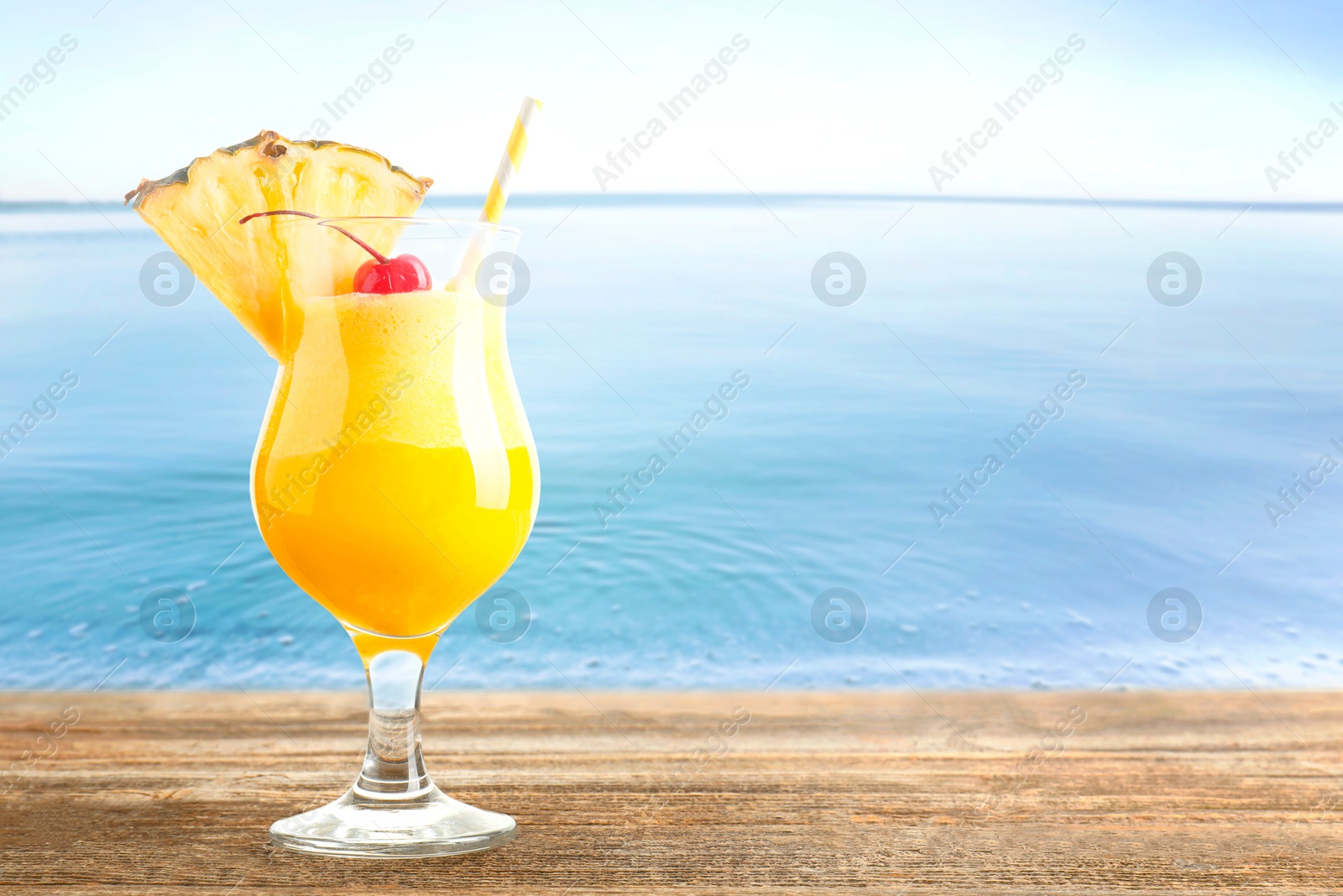 Image of Tasty pineapple cocktail in glass on wooden table against seascape. Space for text