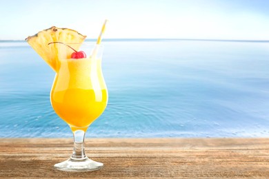 Image of Tasty pineapple cocktail in glass on wooden table against seascape. Space for text