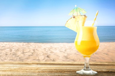 Image of Tasty pineapple cocktail in glass on wooden table against seascape. Space for text