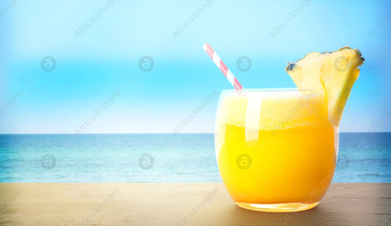 Image of Tasty pineapple cocktail in glass on wooden table against seascape, space for text. Banner design