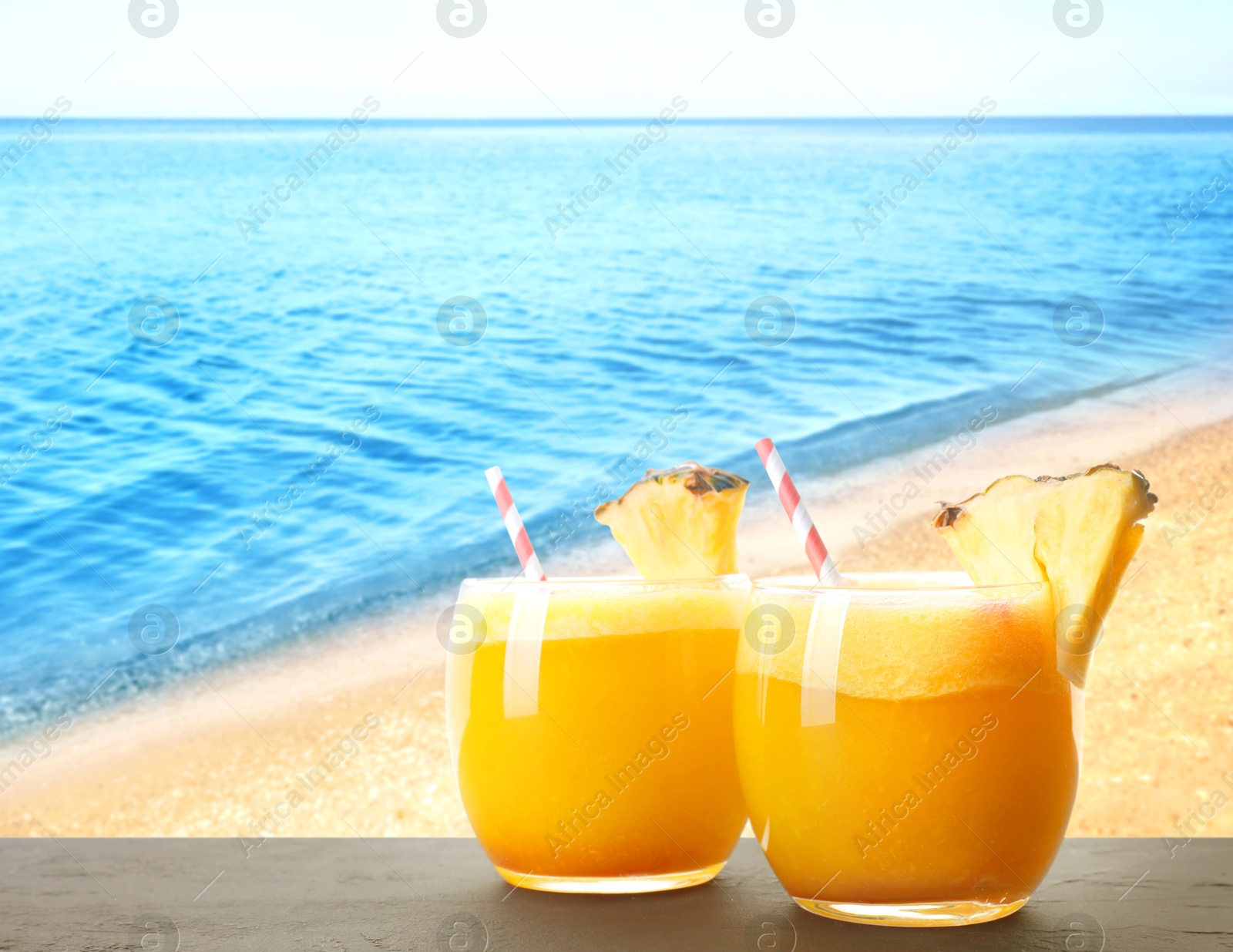 Image of Tasty pineapple cocktail in glasses on wooden table against seascape. Space for text