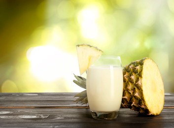 Image of Tasty pineapple cocktail or smoothie in glass and fresh fruit on wooden table outdoors. Space for text