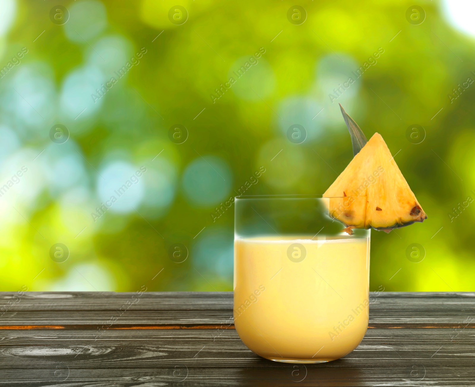 Image of Tasty pineapple cocktail in glass on wooden table outdoors. Space for text