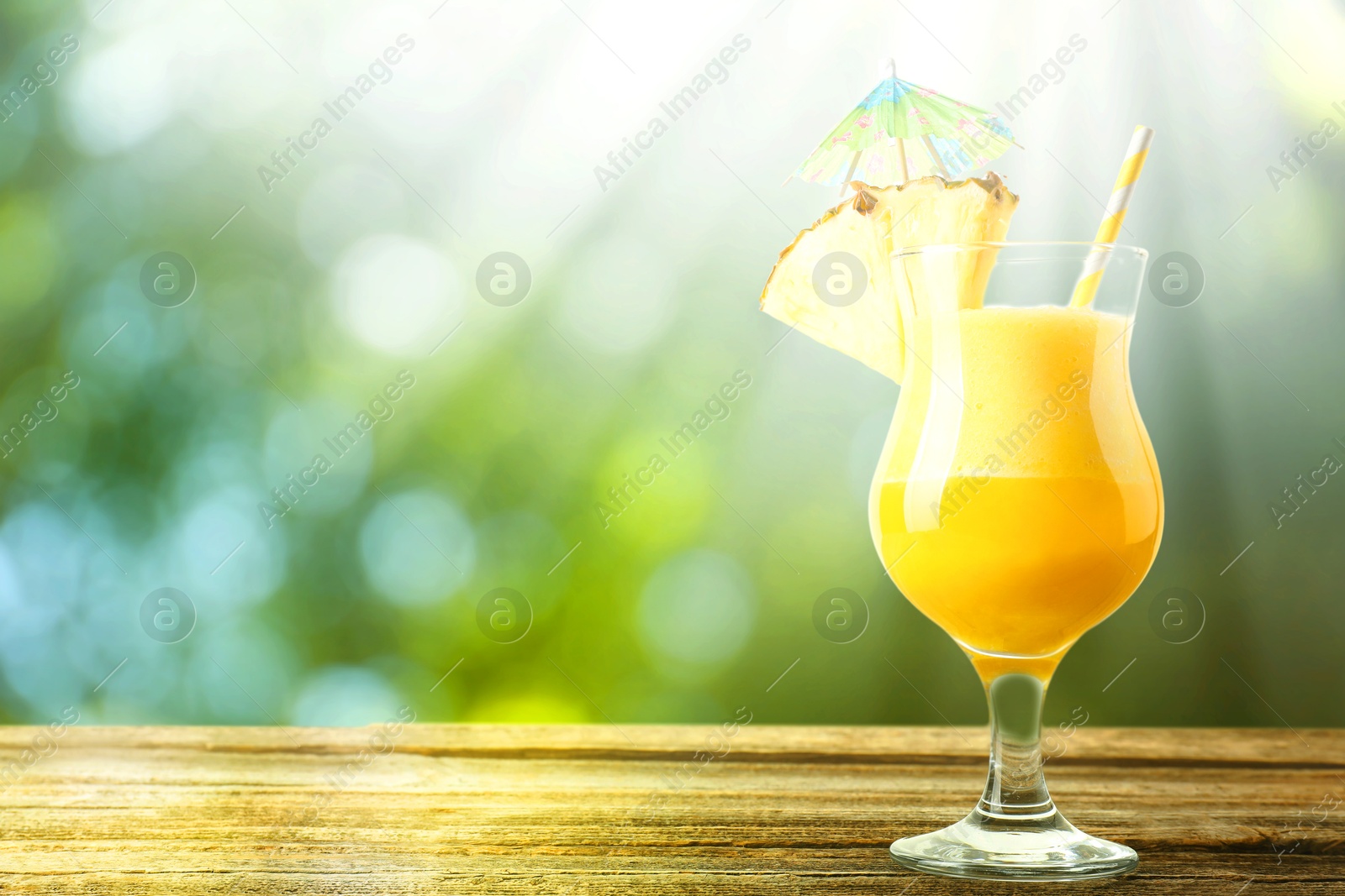 Image of Tasty pineapple cocktail in glass on wooden table outdoors. Space for text