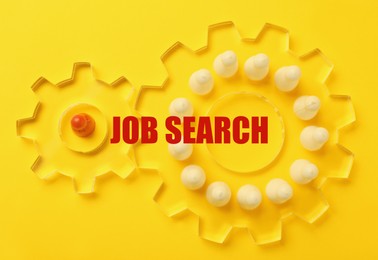 Image of Job search. Game pieces in two transparent cogwheels on yellow background, top view