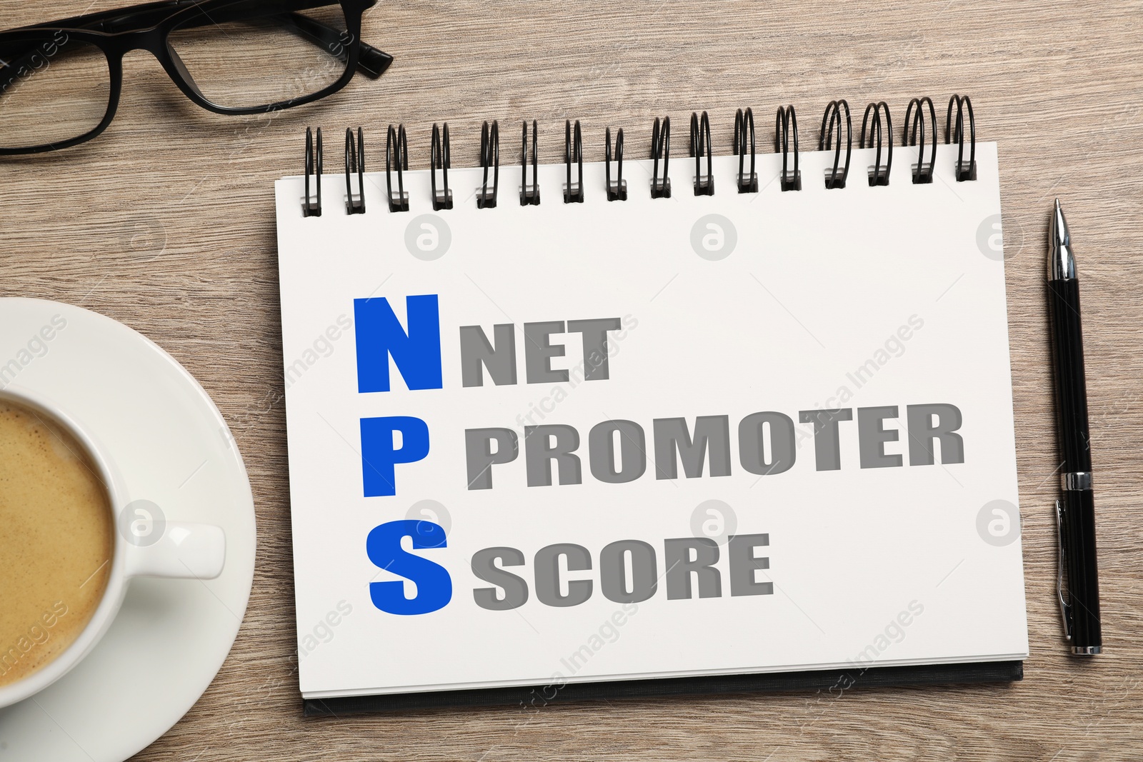 Image of NPS (net promoter score) in notebook, pen, glasses and coffee on wooden table, top view. Customer satisfaction assessment