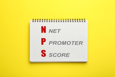 Image of NPS (net promoter score) in notebook on yellow background, top view. Customer satisfaction assessment