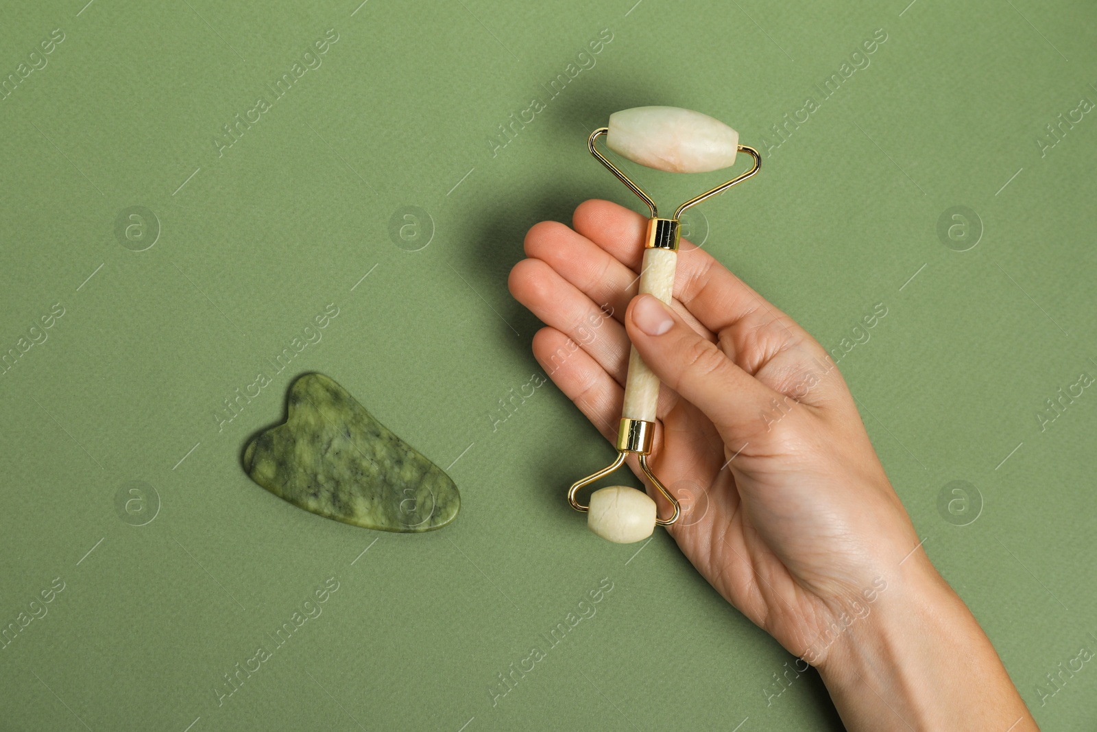 Photo of Woman with face roller and gua sha tool on green background, top view