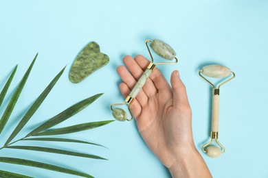 Photo of Woman with face rollers, gua sha tool and leaf on light blue background, top view