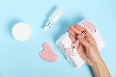 Photo of Woman with face roller, gua sha tool, cosmetic products and towel on light blue background, top view