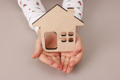 Photo of Adoption. Little girl with house figure at beige table, closeup