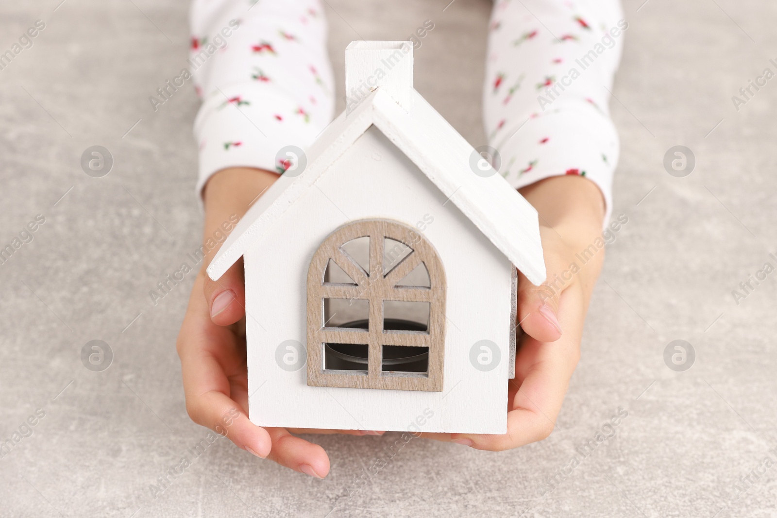 Photo of Adoption. Little girl with house figure at grey table, closeup