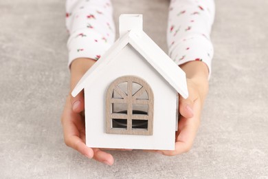 Photo of Adoption. Little girl with house figure at grey table, closeup