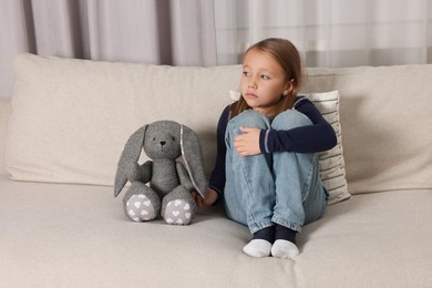 Photo of Autism concept. Lonely little girl with toy bunny on sofa at home