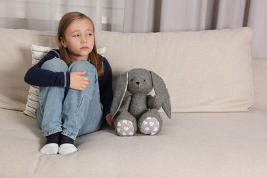 Photo of Autism concept. Lonely little girl with toy bunny on sofa at home