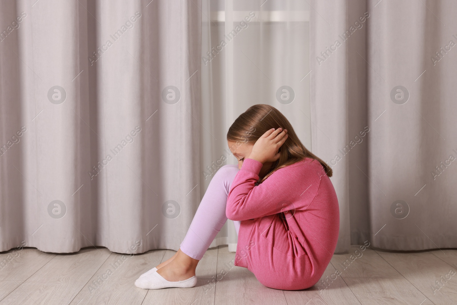 Photo of Autism concept. Scared little girl covering her ears on floor at home