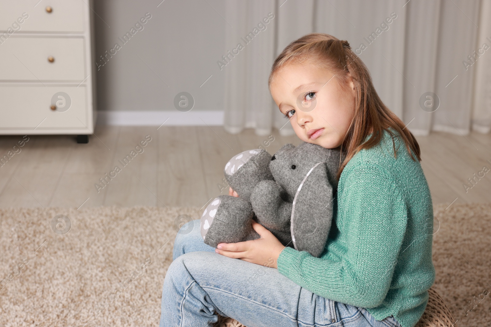 Photo of Autism concept. Lonely little girl with toy bunny on pouf at home, space for text