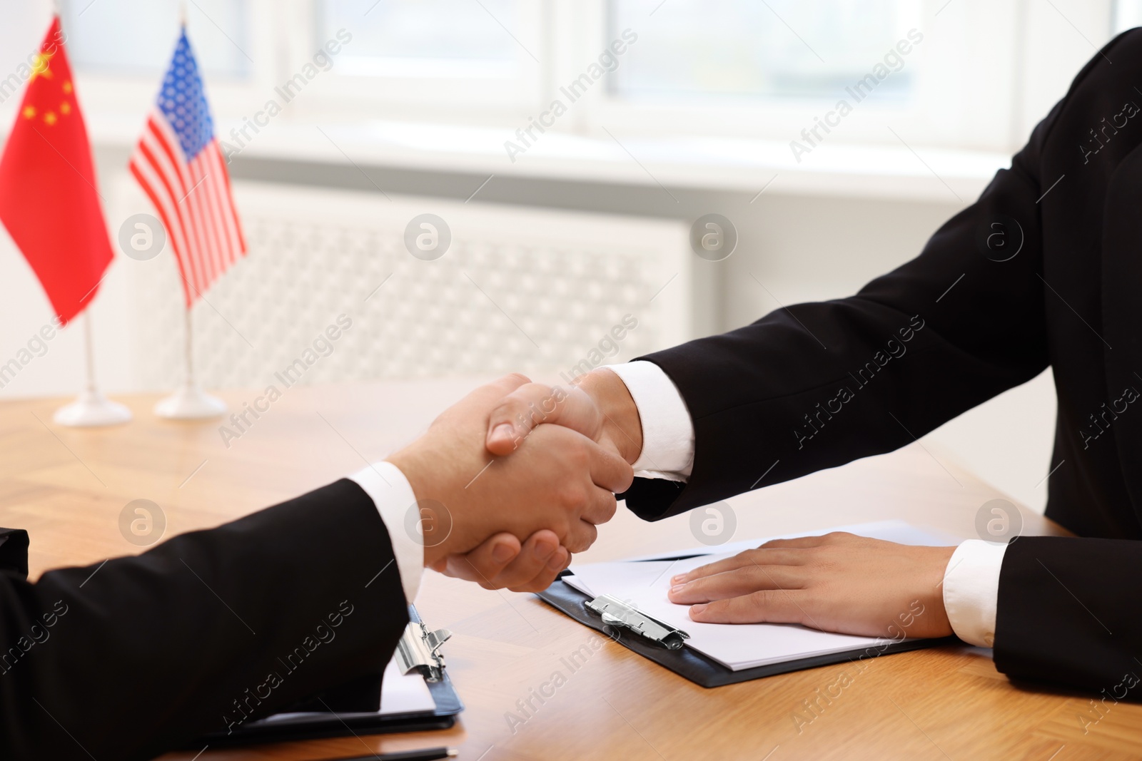 Photo of Diplomats shaking hands during meeting at wooden table indoors, closeup