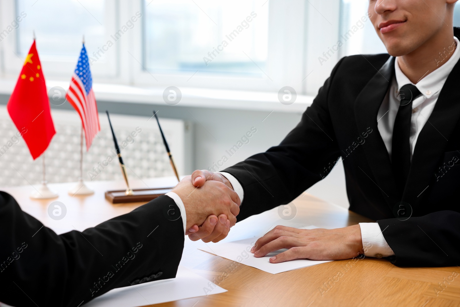 Photo of Diplomats shaking hands during meeting at wooden table indoors, closeup