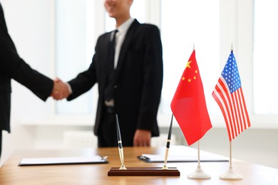 Diplomats shaking hands during meeting indoors, focus on flags of USA and China