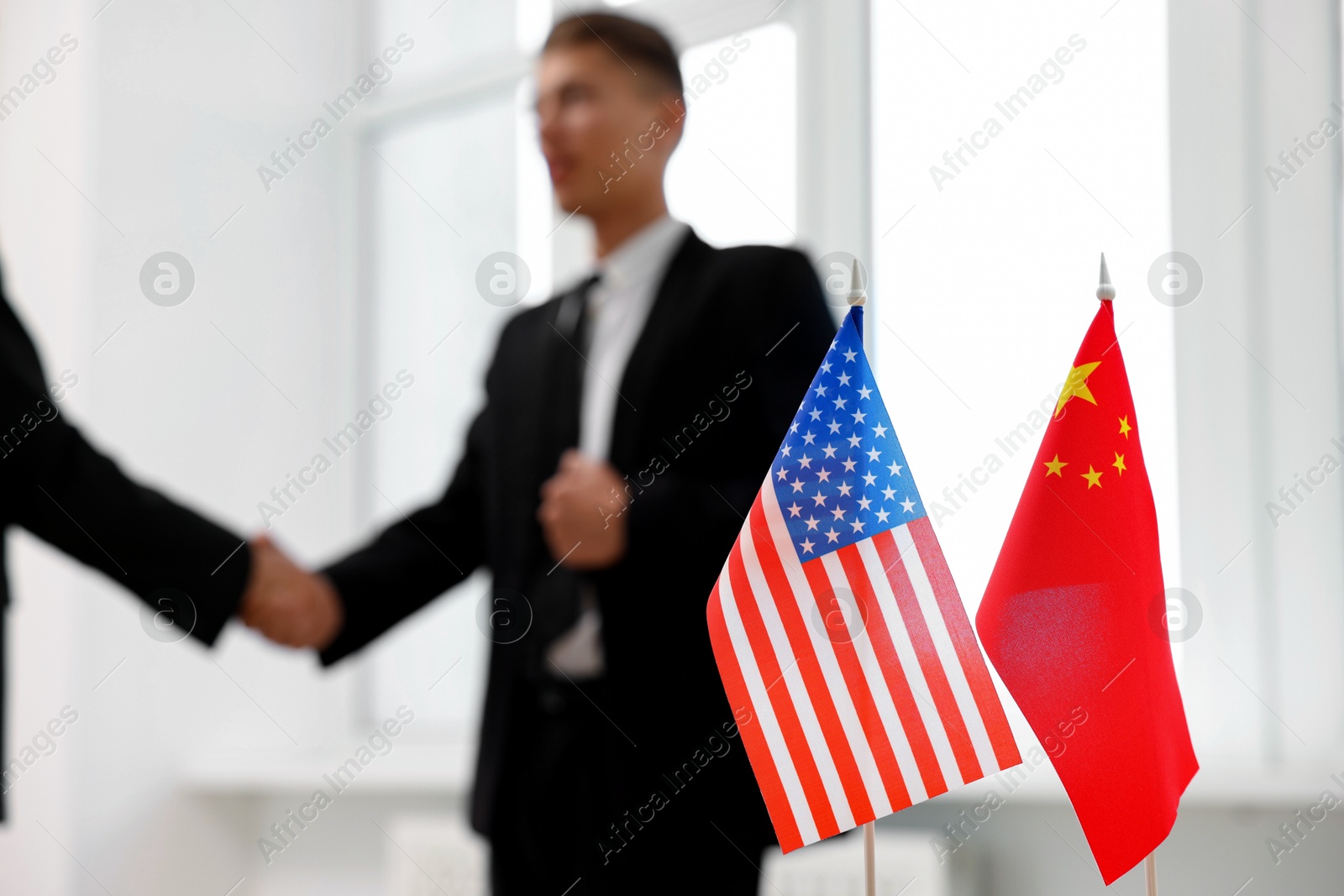 Photo of Diplomats shaking hands during meeting indoors, focus on flags of USA and China