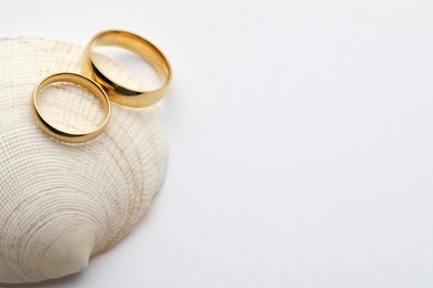 Photo of Beautiful golden wedding rings and sea shell on white background, above view. Space for text