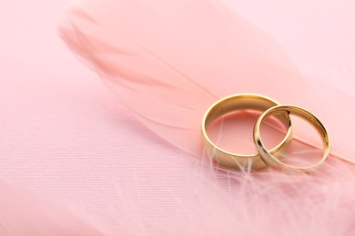 Photo of Beautiful golden wedding rings and feathers on pink background, closeup