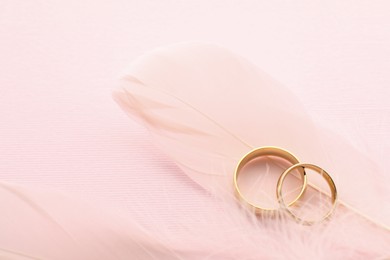 Beautiful golden wedding rings and feathers on pink background, above view