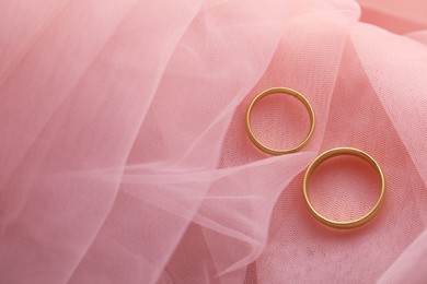 Photo of Beautiful golden wedding rings on pink fabric, top view. Space for text