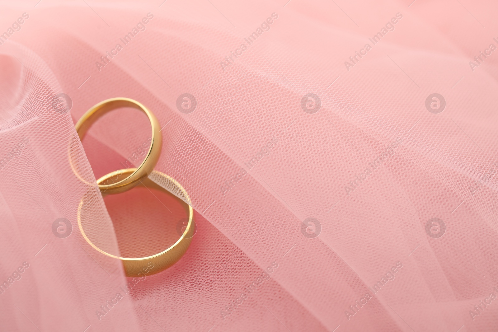 Photo of Beautiful golden wedding rings on pink fabric, space for text