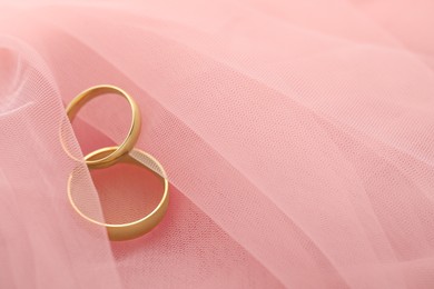 Beautiful golden wedding rings on pink fabric, space for text