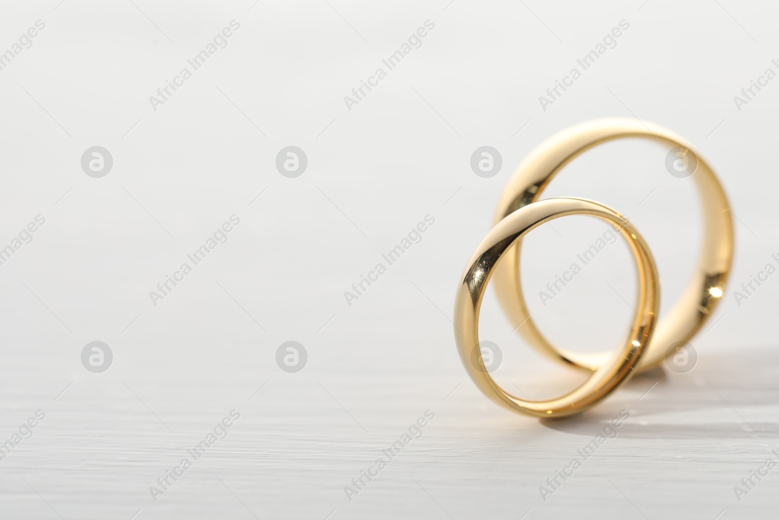 Photo of Beautiful golden wedding rings on light wooden background, space for text