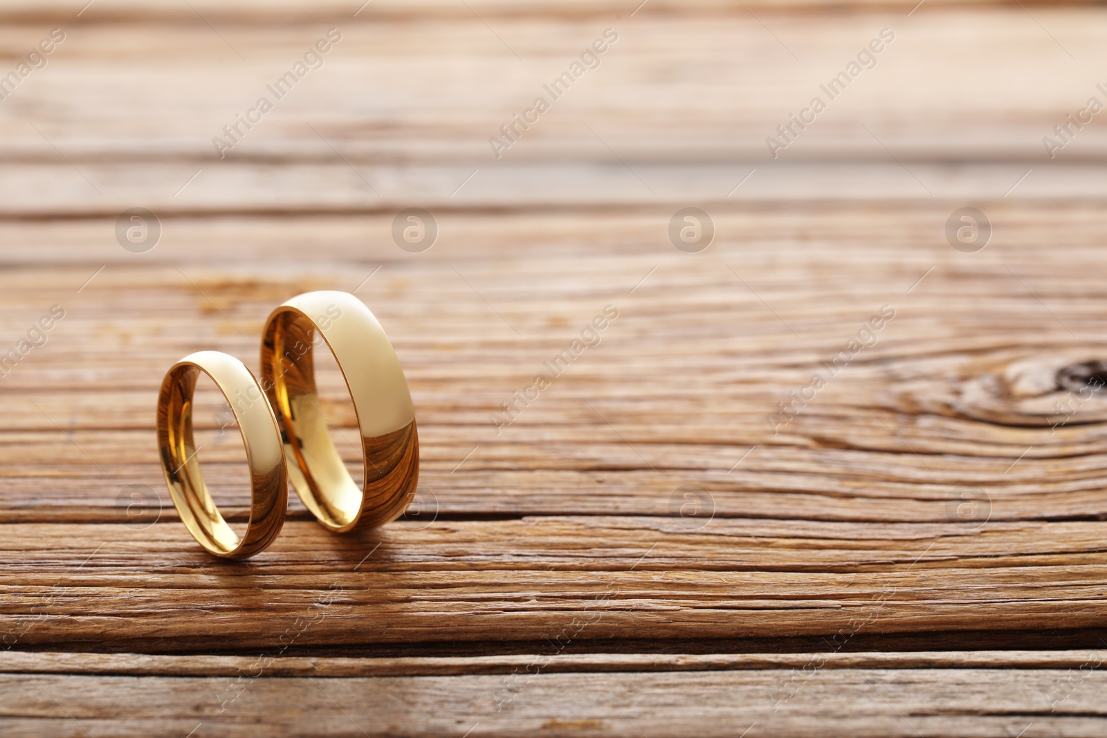 Photo of Beautiful golden wedding rings on wooden background, space for text