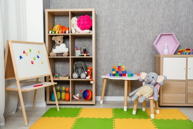 Photo of Beautiful kid's room interior with toys, whiteboard and stylish furniture