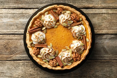 Homemade pumpkin pie with whipped cream, seeds and cinnamon on wooden table, top view