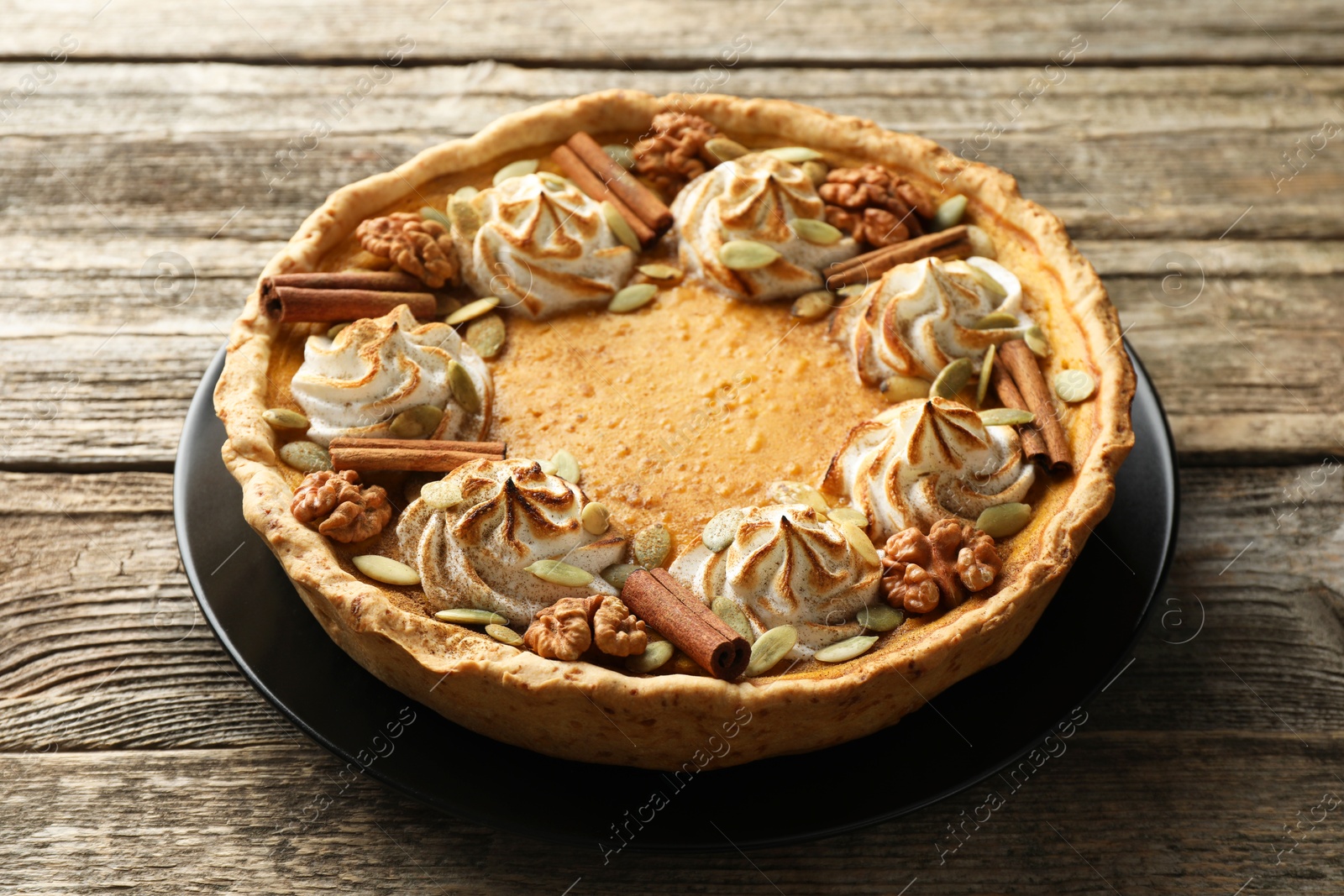 Photo of Homemade pumpkin pie with whipped cream, seeds and cinnamon on wooden table