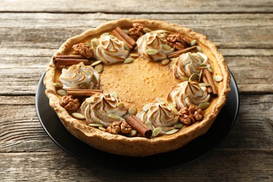 Photo of Homemade pumpkin pie with whipped cream, seeds and cinnamon on wooden table