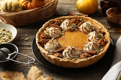 Photo of Homemade pumpkin pie with whipped cream, seeds and cinnamon on wooden table