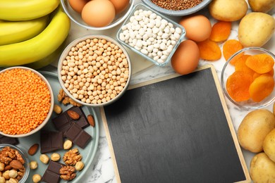 Photo of Anemia diet plan. Different products rich in iron and chalkboard on white marble table, flat lay. Space for text