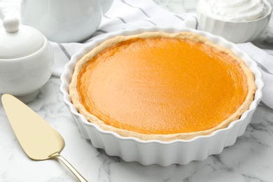 Tasty homemade pumpkin pie and server on white marble table, closeup