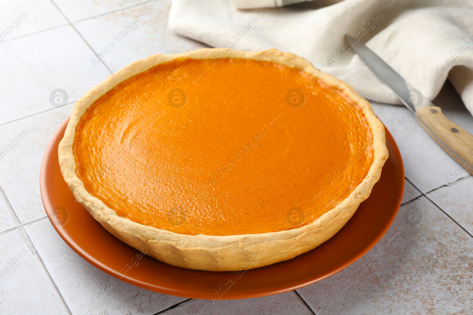 Photo of Tasty homemade pumpkin pie on light tiled table, closeup