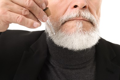 Photo of Senior man applying serum onto his beard on white background, closeup